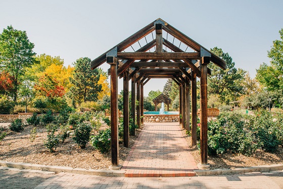 A brick walkway surrounded by a wooden gazebo style walkway leading towards a fountain