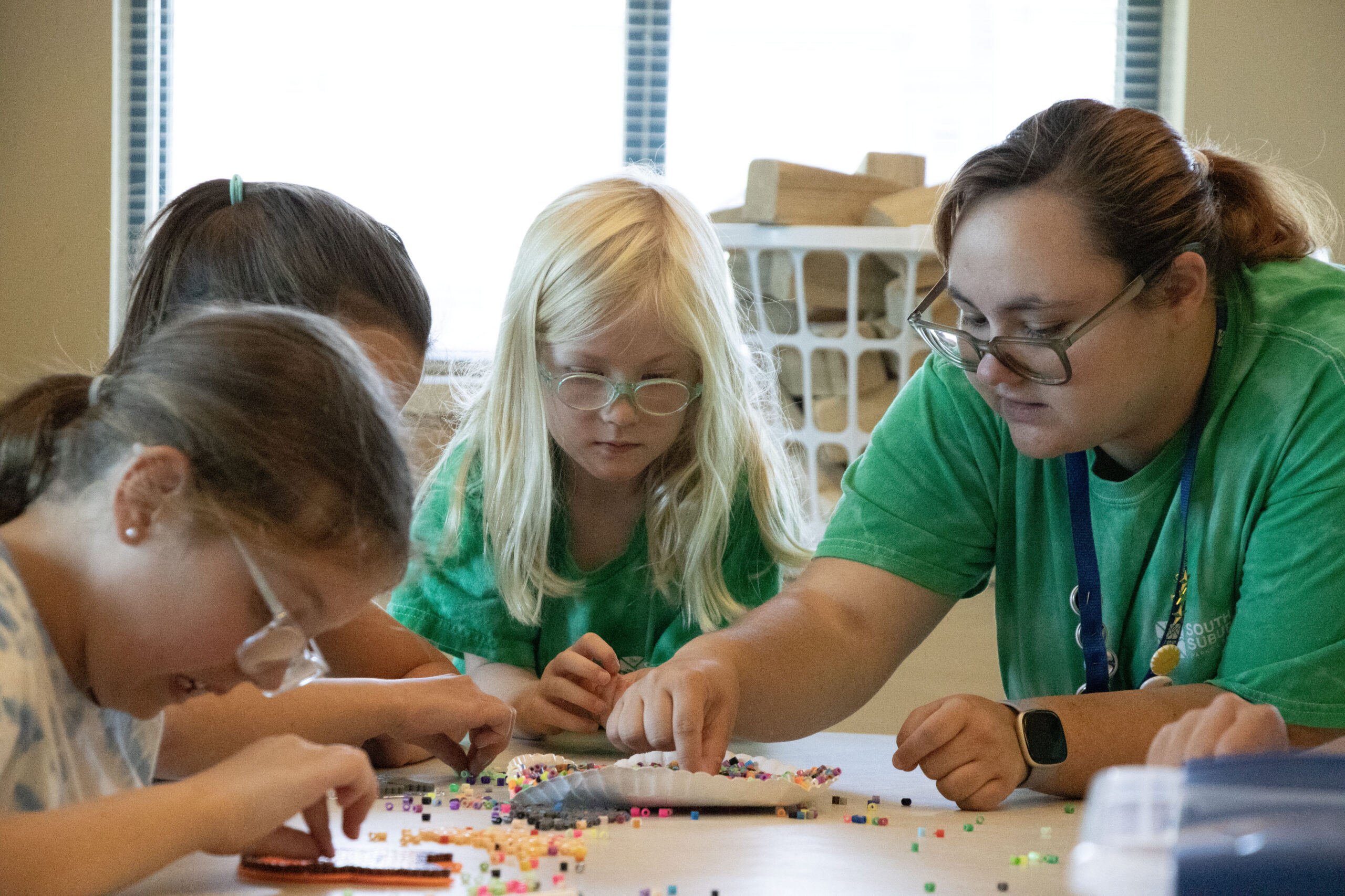 Adult assisting children with beading craft