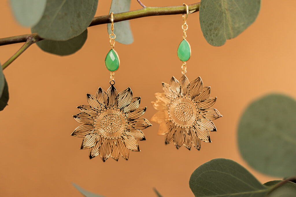 Two gold, flower-shaped earrings displayed hanging from a branch