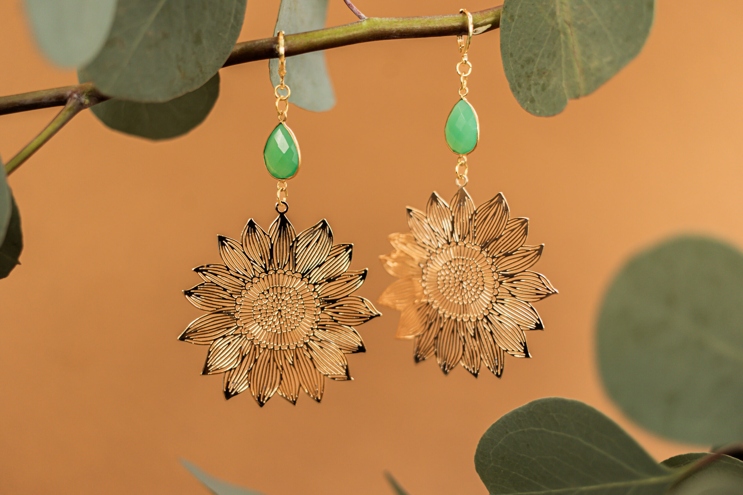 Two gold, flower-shaped earrings displayed hanging from a branch