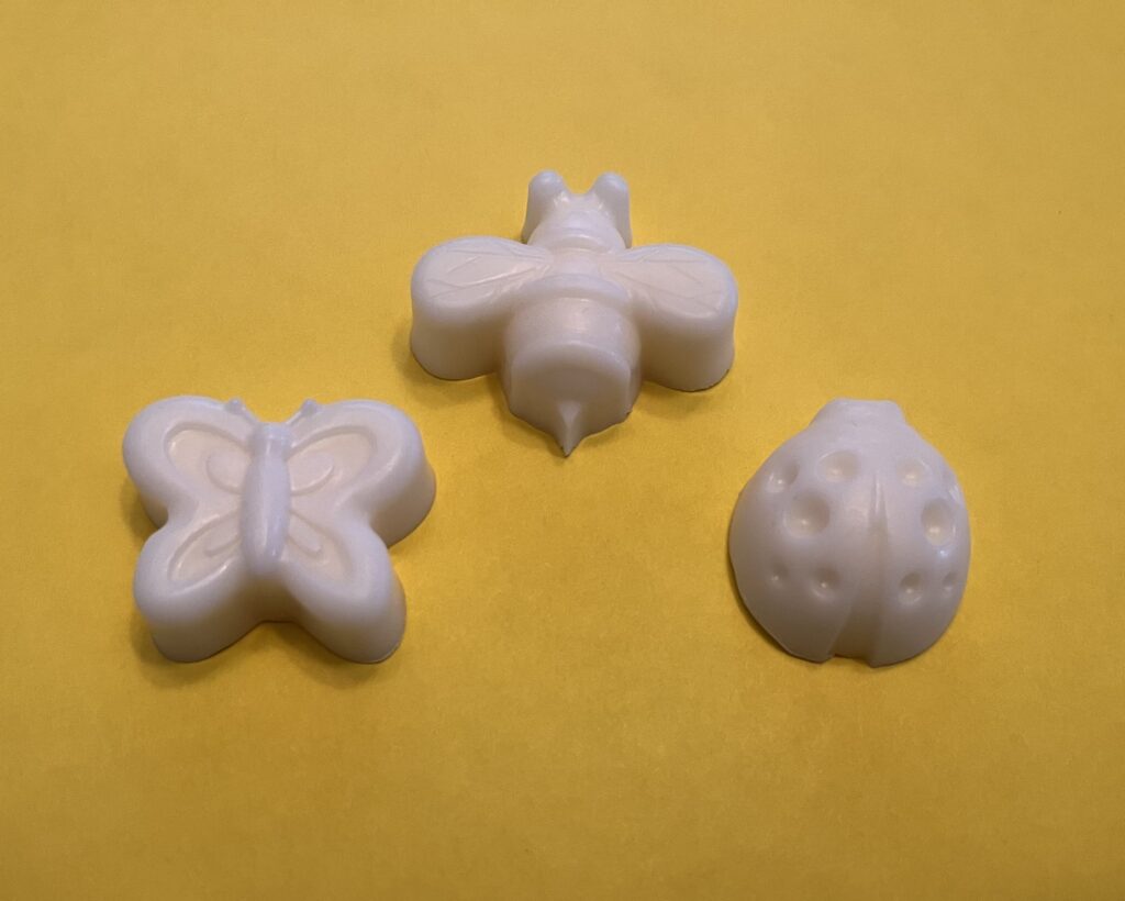 Three handmade soaps in the shape of a butterfly, bee, and ladybug