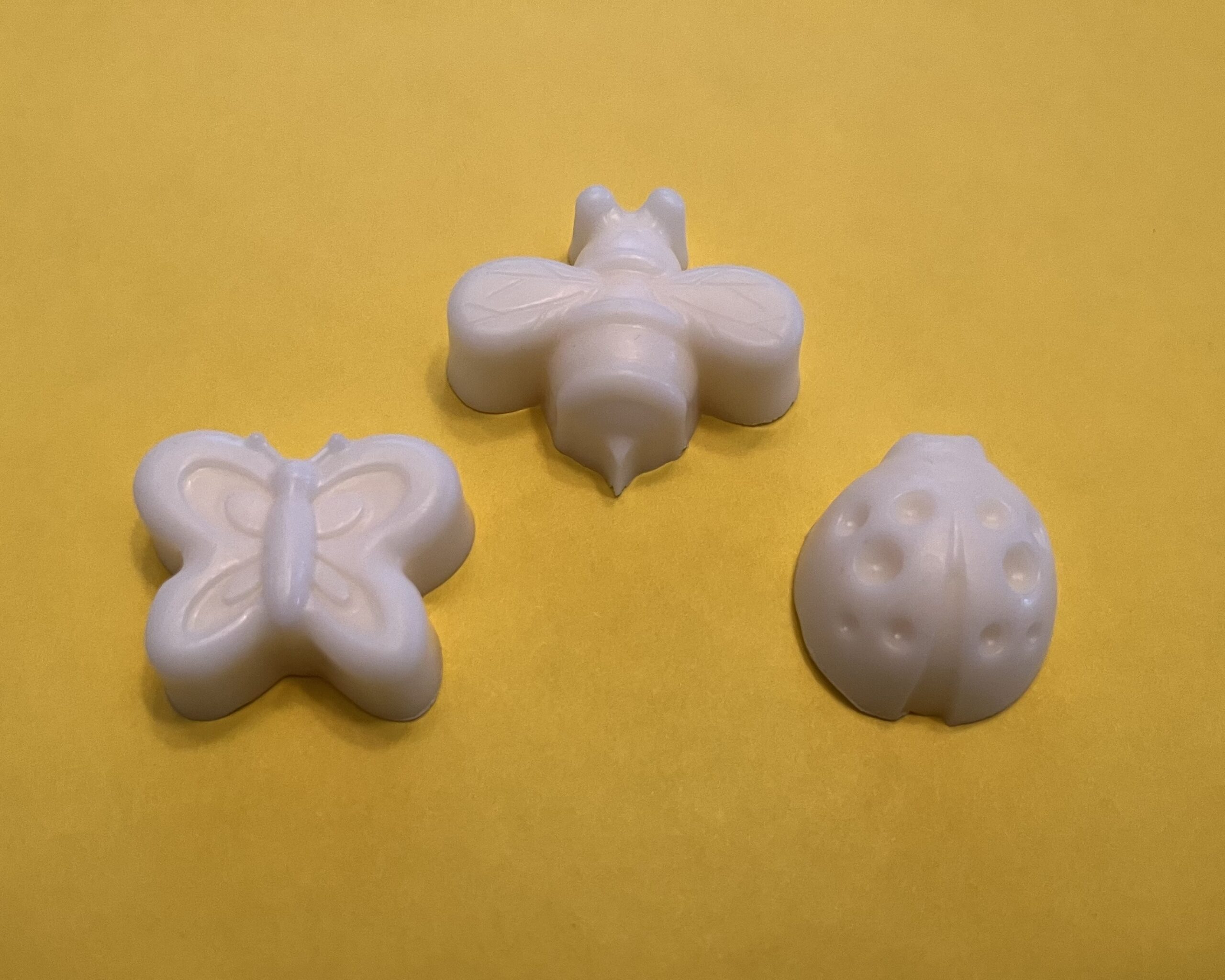 Three handmade soaps in the shape of a butterfly, bee, and ladybug