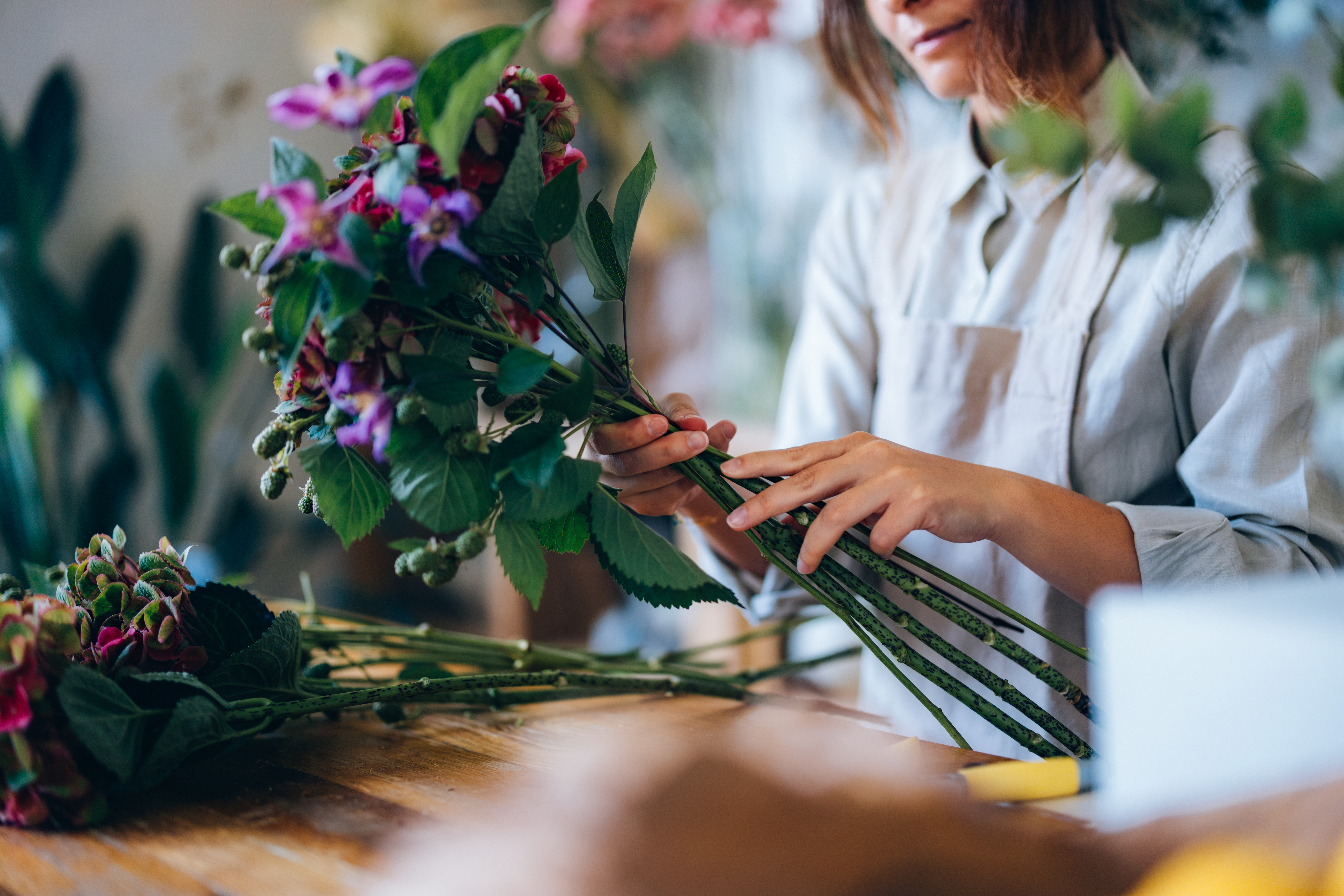 A florist skillfully arranges fresh flowers into a charming bouquet, displaying creativity and care while working in a well-lit, inspiration-filled workspace, surrounded by love for floral art.