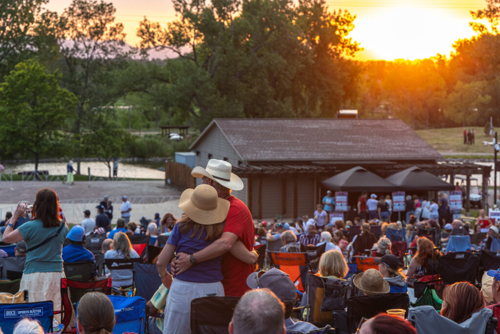Couple with their arms around each other in concert crowd with sunset in the background