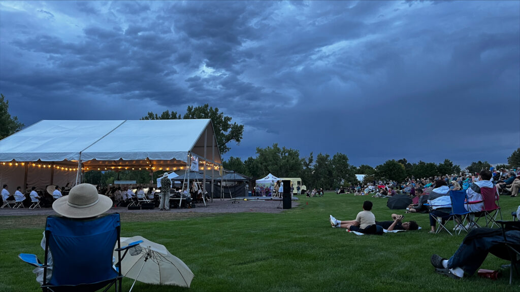 People sitting in lawn chairs watching the symphony play under a large tent