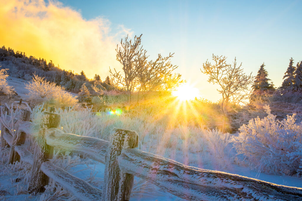 Sunrise over a snowy landscape with a fence in the foreground